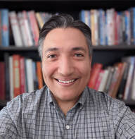 Headshot of George Martinez in front of bookshelf. 